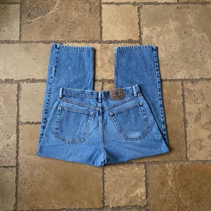 K&ouml;nnte beinhalten: Eine blaue Jeanshose mit einem braunen Leder-Patch am hinteren Bund. Die Jeans hat einen geraden Schnitt und eine lockere Passform.