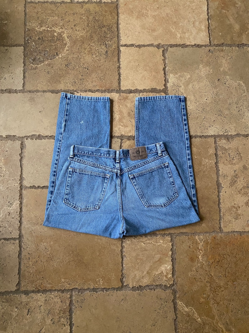 K&ouml;nnte beinhalten: Eine blaue Jeanshose mit einem braunen Leder-Patch am hinteren Bund. Die Jeans hat einen geraden Schnitt und eine lockere Passform.
