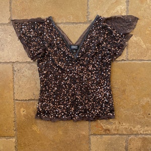 Puede incluir: Una blusa marr&oacute;n de lentejuelas con mangas cortas con volantes y cuello en V. La blusa tiene una etiqueta que dice "Adrianna Papell".