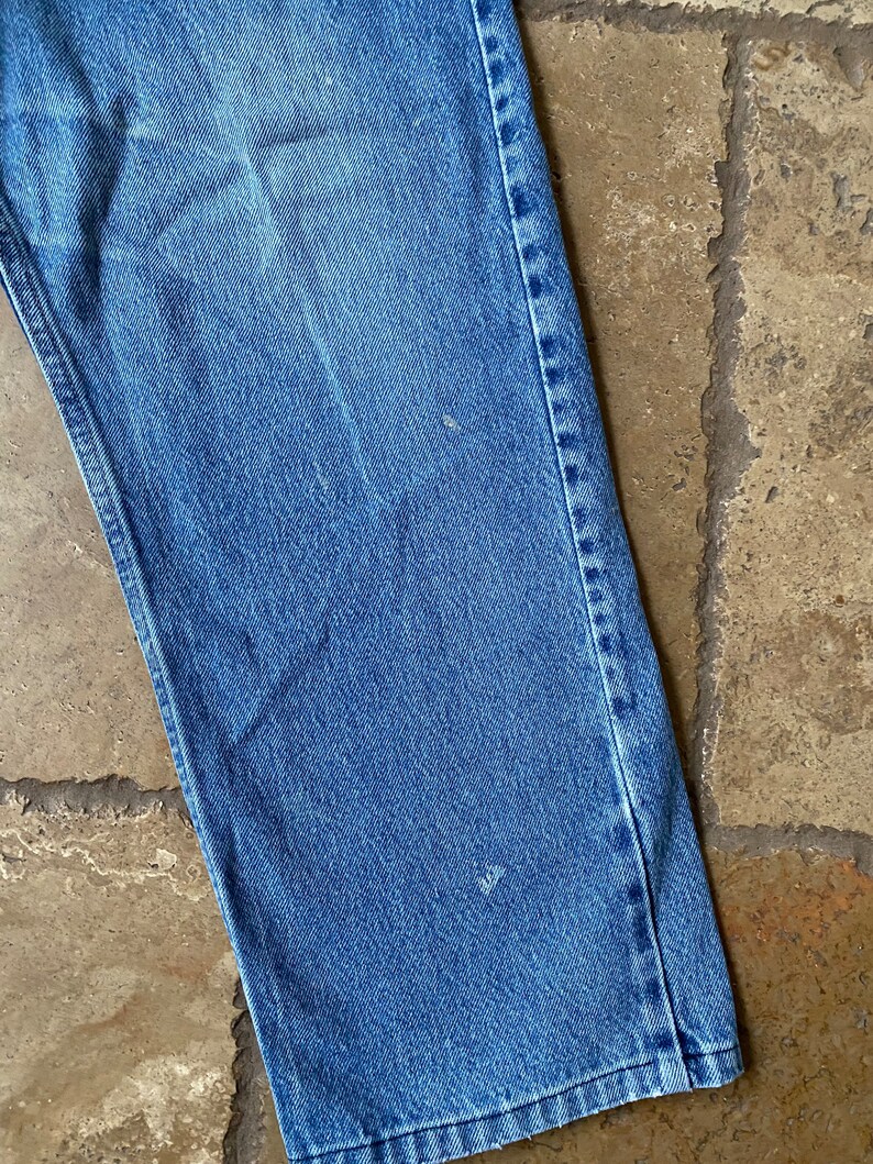 K&ouml;nnte beinhalten: Nahaufnahme des unteren Teils einer blauen Jeans. Der Stoff ist hell gewaschen und die N&auml;hte sind sichtbar.