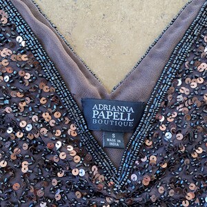 Puede incluir: Una blusa gris oscuro con lentejuelas y escote en V. La etiqueta dice "Adrianna Papell Boutique" y "S Made in India".