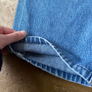 K&ouml;nnte beinhalten: Nahaufnahme des Saums einer blauen Jeans. Der Stoff ist hell gewaschen und die N&auml;hte sind sichtbar.