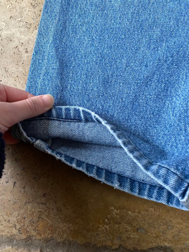 K&ouml;nnte beinhalten: Nahaufnahme des Saums einer blauen Jeans. Der Stoff ist hell gewaschen und die N&auml;hte sind sichtbar.
