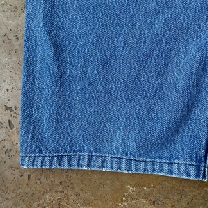 K&ouml;nnte beinhalten: Nahaufnahme des unteren Saums einer blauen Jeans. Der Stoff ist ein klassischer Jeansstoff mit leicht verblassten Look.