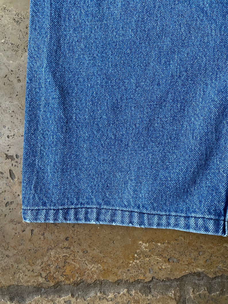 K&ouml;nnte beinhalten: Nahaufnahme des unteren Saums einer blauen Jeans. Der Stoff ist ein klassischer Jeansstoff mit leicht verblassten Look.