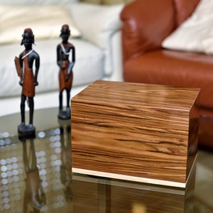 May include: A wooden box with a light brown wood grain pattern. The box has a light brown wood trim around the edges. The box is sitting on a glass table.