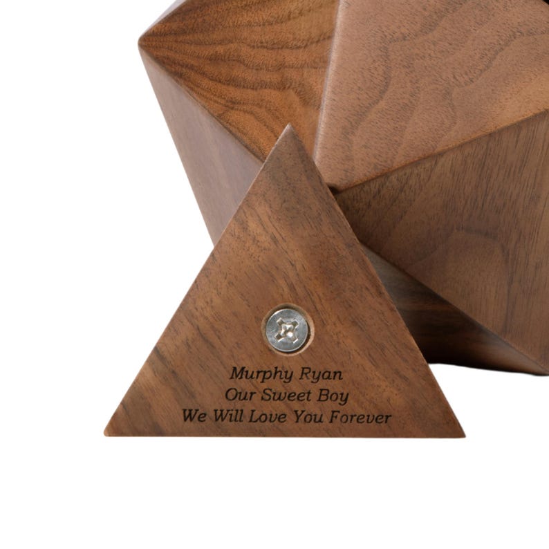 May include: A wooden geometric box with a triangular base. The box is engraved with the words "Murphy Ryan Our Sweet Boy We Will Love You Forever".