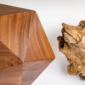 May include: A geometric wooden sculpture made of walnut wood. The sculpture has a faceted, multi-sided shape. The wood has a rich brown color and a natural grain pattern.
