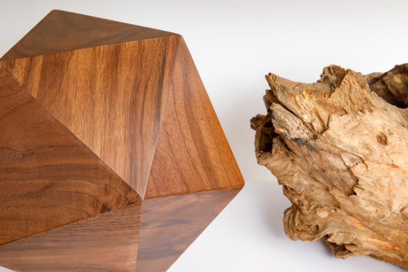 May include: A geometric wooden sculpture made of walnut wood. The sculpture has a faceted, multi-sided shape. The wood has a rich brown color and a natural grain pattern.