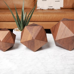 May include: Three geometric wooden sculptures in various sizes, made of dark brown walnut wood, sitting on a white marble surface.
