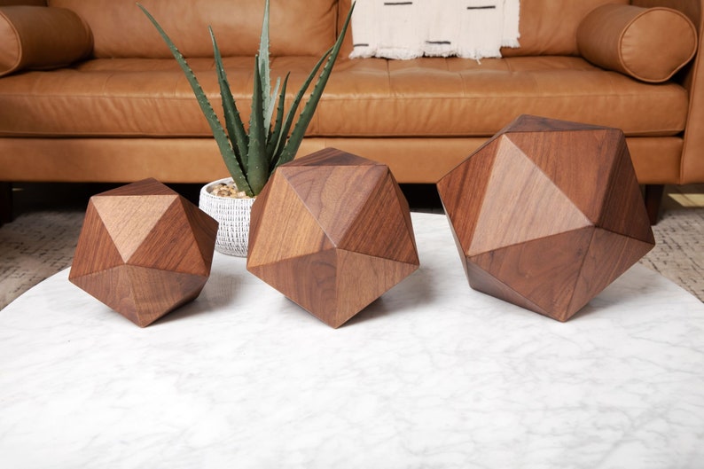 May include: Three geometric wooden sculptures in various sizes, made of dark brown walnut wood, sitting on a white marble surface.