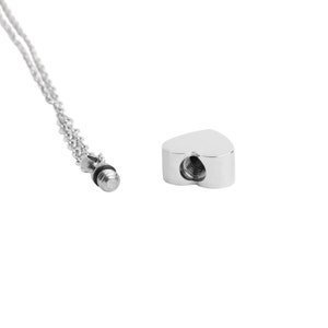 May include: A silver heart-shaped cremation necklace with a threaded screw closure. The necklace is on a silver chain.