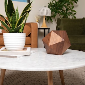 May include: A white marble coffee table with a wooden geometric sculpture on top. The table has a round top and three wooden legs. The sculpture is made of dark wood and has a geometric shape.