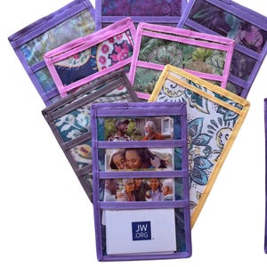Puede incluir: Una colección de organizadores rectangulares de tela con ventanas de vinilo transparente y bordes de tela morados, amarillos o rosas. Cada organizador tiene varias ranuras horizontales con fotografías impresas y una tarjeta con el texto JW.ORG.