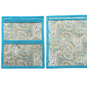 Pu&ograve; includere: Due presine rettangolari in tessuto con motivo paisley nei toni del verde salvia, beige e azzurro. Ogni articolo &egrave; rifinito con un bordo in tessuto blu turchese brillante lungo i lati e include un dettaglio a tasca orizzontale.