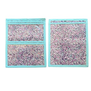 Pu&ograve; includere: Due organizer rettangolari in tessuto con bordo azzurro e un fitto motivo floreale con fiori rosa, viola e bianchi. Un organizer presenta due tasche orizzontali in plastica trasparente, l'altro ha un'unica grande tasca trasparente.