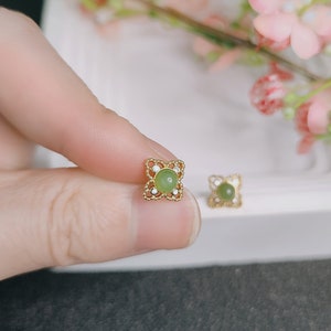 Puede incluir: Un par de pendientes de oro con una piedra verde en el centro de cada pendiente. Los pendientes tienen forma de trébol de cuatro hojas.