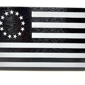 May include: Rectangular black and white flag design with a circle of 13 white stars in the upper left corner. The flag has alternating horizontal white and black stripes. The flag is on a white background.