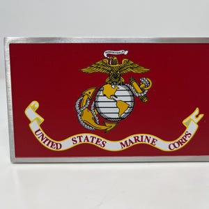 May include: Metal belt buckle with a red background. The buckle features the United States Marine Corps emblem, including an eagle, globe, and anchor, with the words "United States Marine Corps" and "Semper Fidelis".