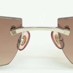 May include: A pair of silver-toned sunglasses with brown gradient lenses and pink earpieces.