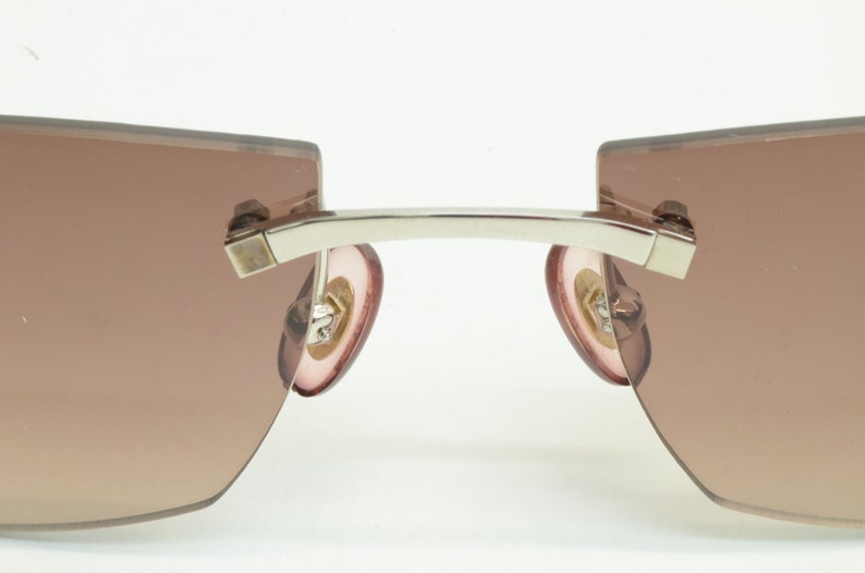 May include: A pair of silver-toned sunglasses with brown gradient lenses and pink earpieces.