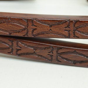 May include: Two brown leather straps with an intricate carved design. The design features a repeating pattern of ovals and swirls.