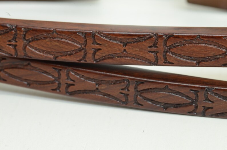 May include: Two brown leather straps with an intricate carved design. The design features a repeating pattern of ovals and swirls.