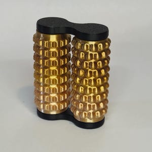 May include: A gold-coloured, double-sided, handheld massage roller with black plastic ends. The roller has a textured surface with raised bumps.