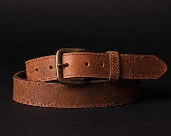 May include: A brown leather belt with a brass buckle. The belt has a stitched edge and is rolled up.