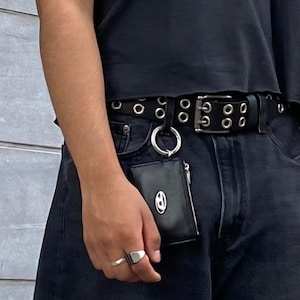May include: A black leather wallet with a silver ring and a silver chain attached. The wallet is hanging from a black belt with silver grommets.