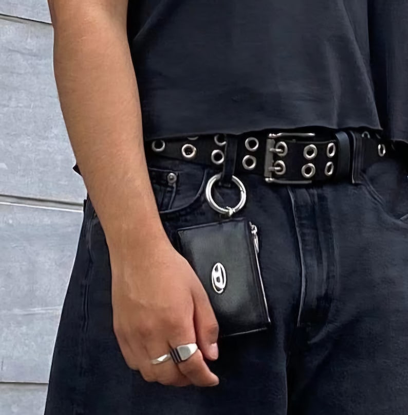May include: A black leather wallet with a silver ring and a silver chain attached. The wallet is hanging from a black belt with silver grommets.