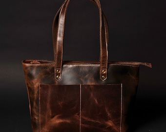 May include: A brown leather tote bag with two top handles and a zip closure. The bag has a distressed look and features a front pocket.