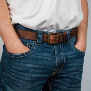 Peut inclure: Une ceinture en cuir marron avec une boucle en laiton, portée sur un jean bleu.
