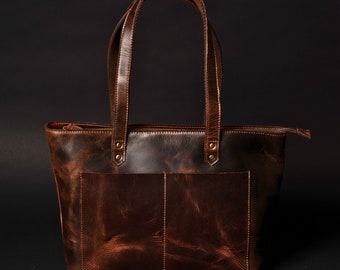 May include: A brown leather tote bag with two top handles and a zip closure. The bag has a distressed look and a front pocket.