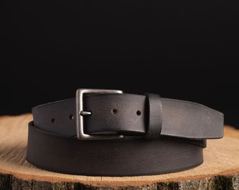 May include: A black leather belt with a silver buckle. The belt is folded and placed on a wooden surface.