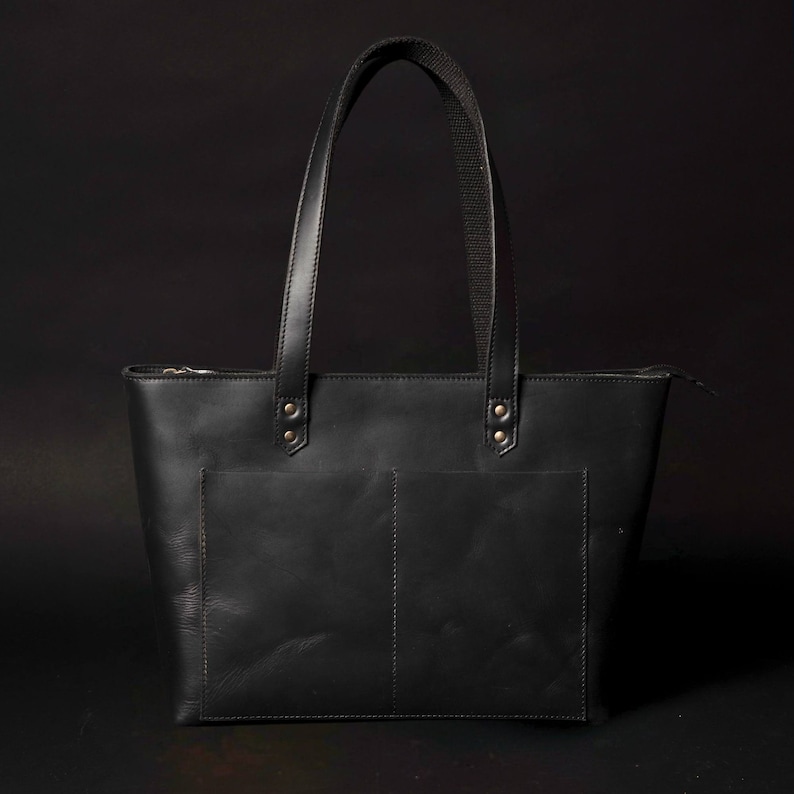 May include: A black leather tote bag with two front pockets and a zip closure. The bag has two top handles.