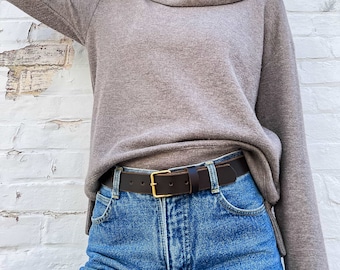 May include: A brown turtleneck sweater with a brown leather belt with a gold buckle. The sweater is worn over a pair of blue jeans.