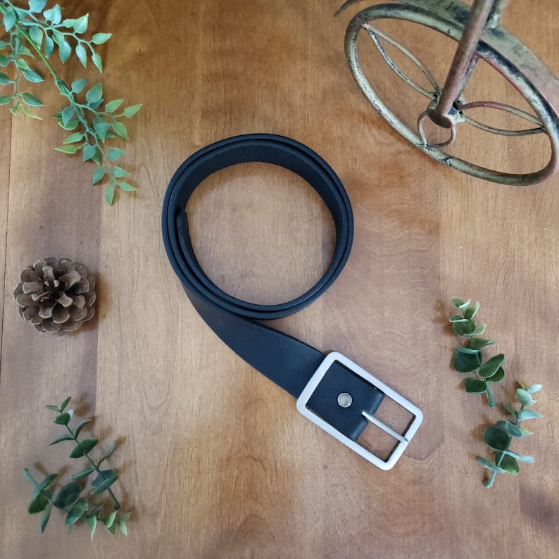 Peut inclure: Une ceinture en cuir noir avec une boucle argent&eacute;e. La ceinture est sur une surface en bois.