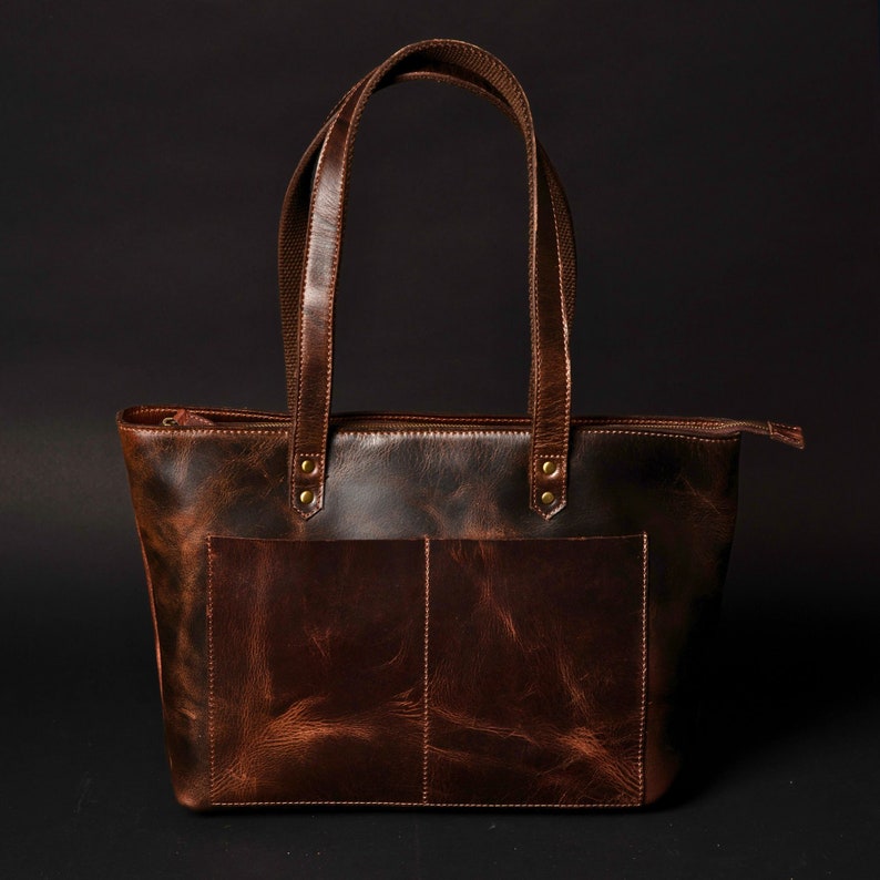 May include: A brown leather tote bag with two top handles and a zip closure. The bag has a distressed look and a front pocket.