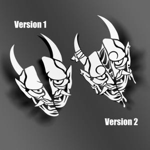 Könnte beinhalten: Zwei weiße, stilisierte Dämonenmasken mit Hörnern und scharfen Zähnen, beschriftet mit "Version 1" und "Version 2" in weißem Text. Die Masken sind vor einem dunkelgrauen Hintergrund platziert, mit Schatten, die einen 3D-Effekt suggerieren.