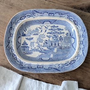 Puede incluir: Plato ovalado de cerámica azul y blanca con diseño Willow. El plato presenta una escena de paisaje detallada con pagodas, puentes y barcos. El borde tiene un patrón decorativo. Una pieza clásica para servir o exhibir.