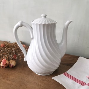 Può includere: Caffettiera in ceramica bianca con un design a spirale e un coperchio. La caffettiera ha un manico e un beccuccio.