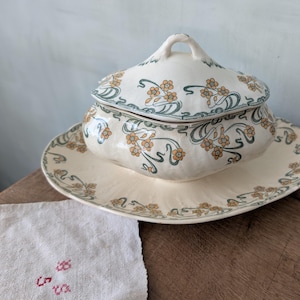 Può includere: Una salsiera in porcellana bianca vintage con coperchio. La salsiera e il coperchio sono decorati con un motivo floreale in tonalità di verde e giallo.