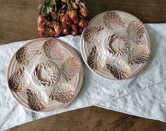 Può includere: Due piatti per ostriche in ceramica vintage con un design a forma di granchio al centro. I piatti sono bianchi con accenti marroni e beige.