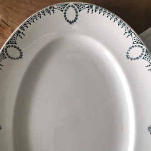 Könnte beinhalten: Eine weiße ovale Servierplatte mit einem grün-weißen Dekorrand. Der Rand zeigt ein sich wiederholendes Muster aus stilisierten Blättern und geometrischen Formen.