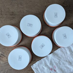 以下が含まれることがあります： 茶色の縁取りが付いた白いセラミック製のラメイクインが5つあります。各ラメイクインには、「PORCELAIN MADE IN FRANCE」というラベルが付いています。