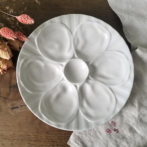 Puede incluir: Plato de ostras de cerámica blanca con seis hendiduras individuales para servir ostras. El plato tiene un borde acanalado y un centro elevado.