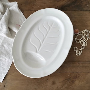 May include: White oval serving platter with a raised leaf design. The platter has a small indentation for sauces or dips.