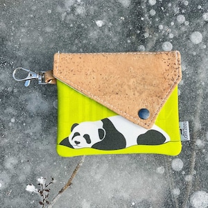 May include: A small, lime green wallet with a panda bear illustration. The wallet has a cork flap and a silver-colored clasp. The panda is black and white and is lying down. The wallet is closed with a black snap.