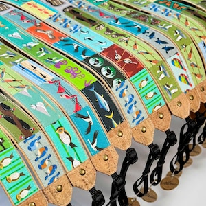 Peut inclure: Plusieurs sangles d'appareil photo colorées avec des motifs d'oiseaux. Les sangles ont une base en liège et un tissu avec des illustrations d'oiseaux, de poissons et d'autres motifs sur le thème de la nature. Chaque sangle a une boucle noire réglable et une petite étiquette.
